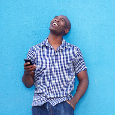 Portrait of smiling african man with a mobile phone standing against blue background